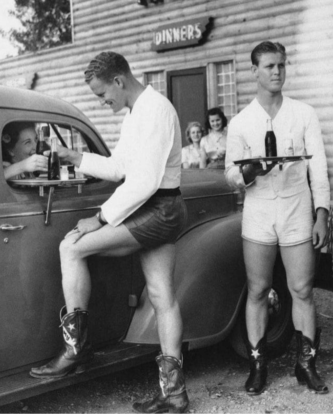 Men waiters in shorts and cowboy boots serve women at the Log Lodge Tavern drive-through in Dallas, Texas, 1940s 
